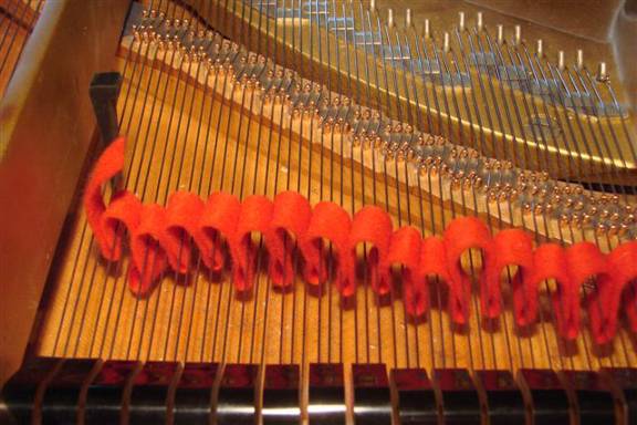 Múltiplos tricordes silenciados num piano de cauda com uma fita de feltro